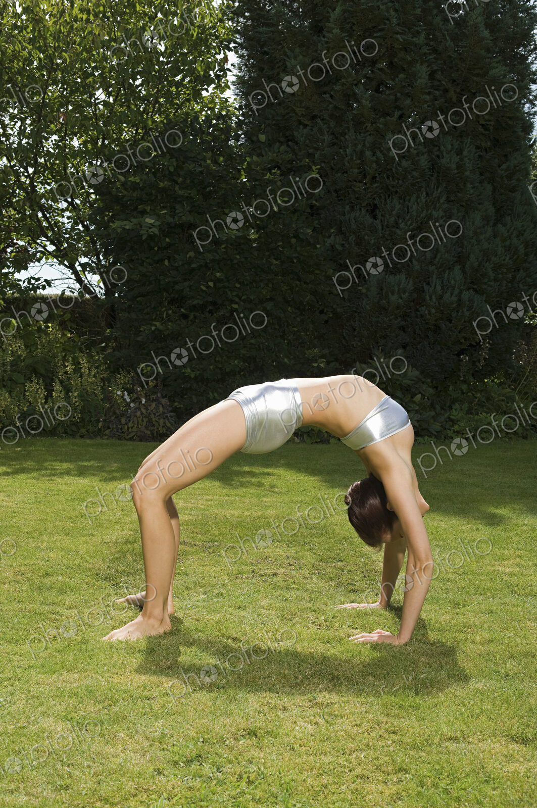 A young woman showing her flexibility, leaning backwards in an arch with hands and…