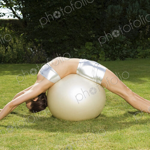 A young woman showing her flexibility, leaning backwards over an exercise ball, with… A young woman showing her flexibility, leaning backwards over an exercise ball, with…