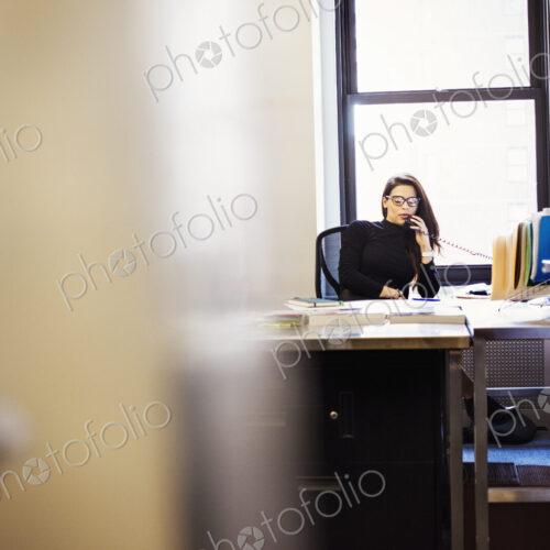 A young woman sitting at a desk in an office holding a telephone to her head. A young woman sitting at a desk in an office holding a telephone to her head.