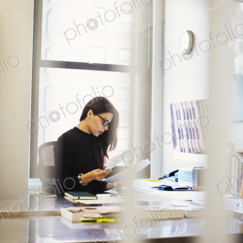 A young woman sitting at a desk in an office looking at paperwork. A young woman sitting at a desk in an office looking at paperwork.