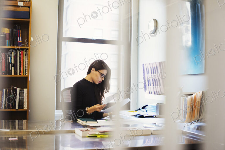 A young woman sitting at a desk in an office looking at paperwork.