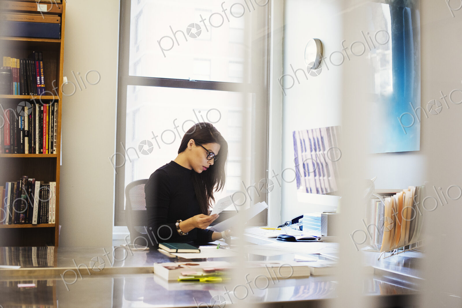 A young woman sitting at a desk in an office looking at paperwork.