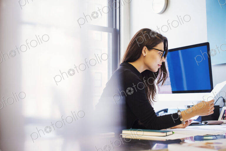 A young woman sitting at a desk in an office looking at paperwork.