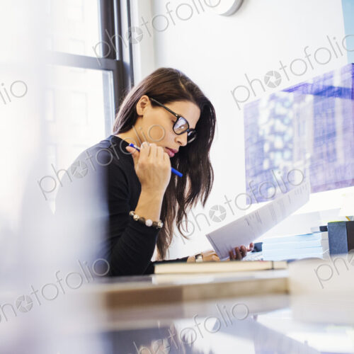 A young woman sitting at a desk in an office looking at paperwork. A young woman sitting at a desk in an office looking at paperwork.