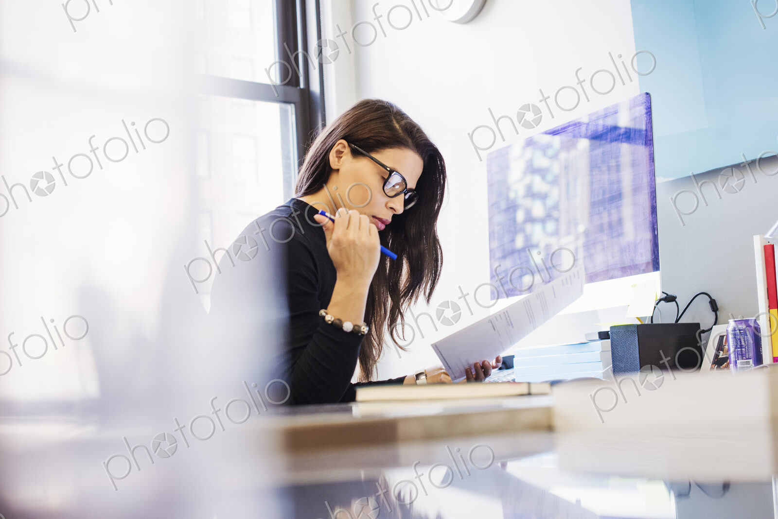 A young woman sitting at a desk in an office looking at paperwork.