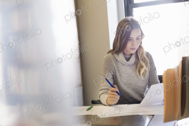 A young woman sitting at a desk in an office looking at paperwork.