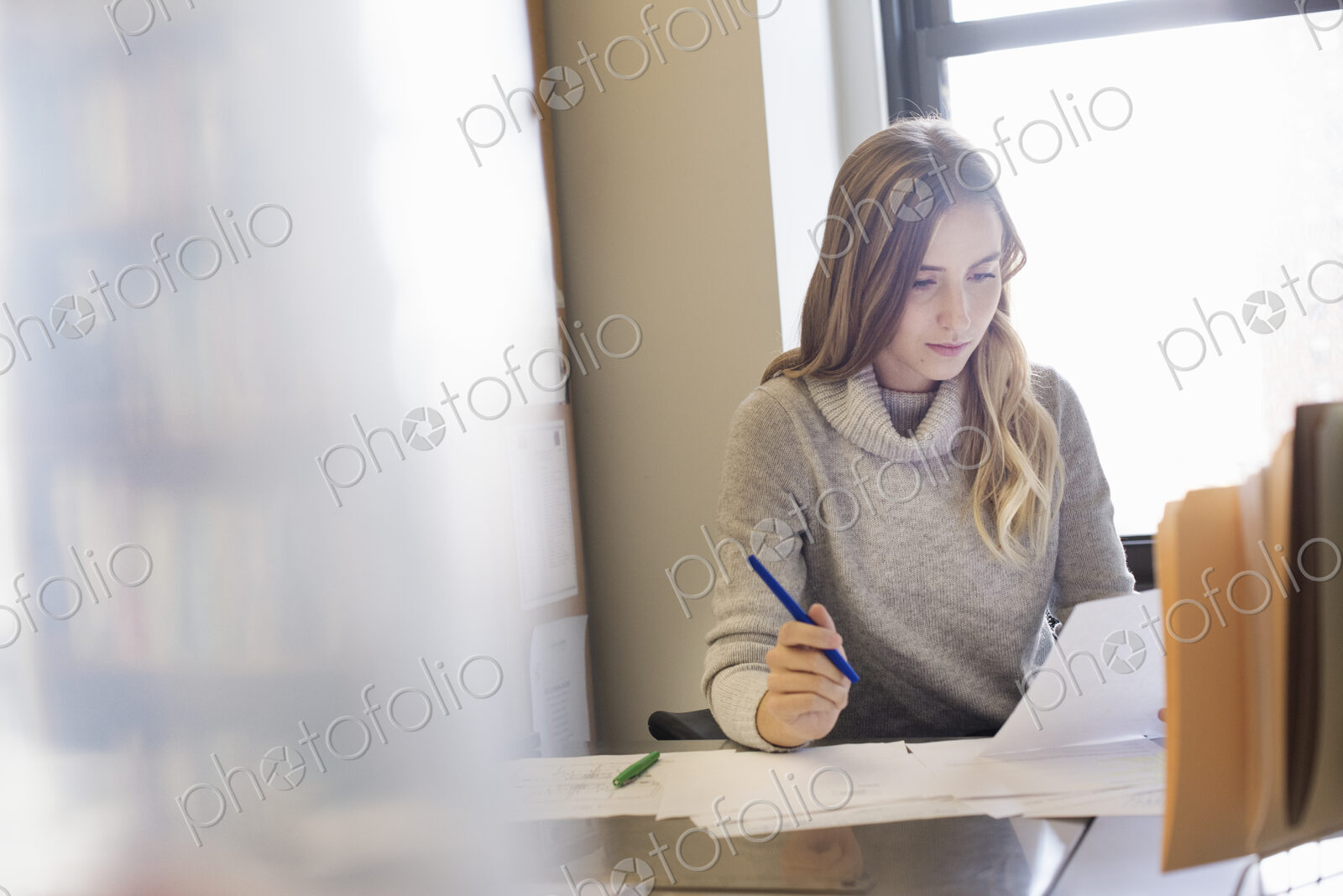 A young woman sitting at a desk in an office looking at paperwork.