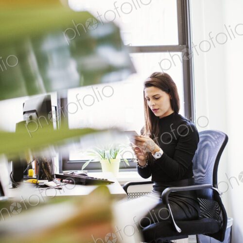 A young woman sitting at a desk in an office looking down at a cellphone. A young woman sitting at a desk in an office looking down at a cellphone.