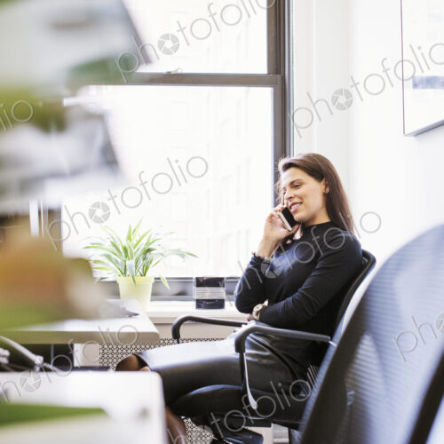 A young woman sitting at a desk with a cellphone to her ear. A young woman sitting at a desk with a cellphone to her ear.
