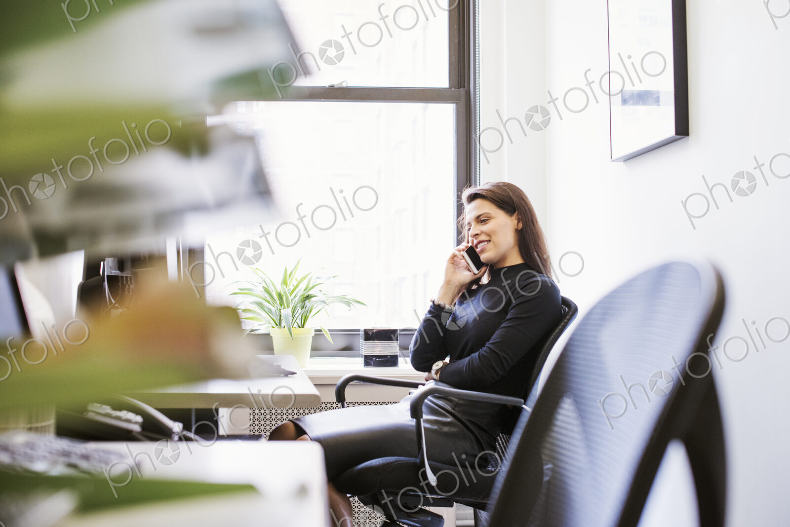 A young woman sitting at a desk with a cellphone to her ear.