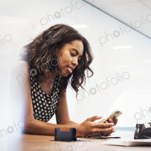 A young woman sitting in a classroom at a table and looking down at a cellphone.