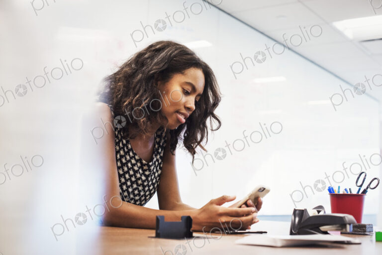 A young woman sitting in a classroom at a table and looking down at a cellphone.