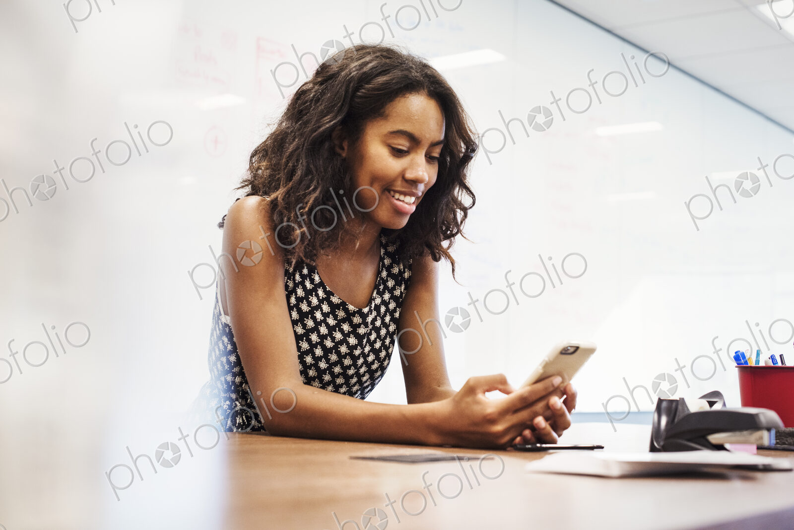 A young woman sitting in a classroom at a table and looking down at a cellphone.