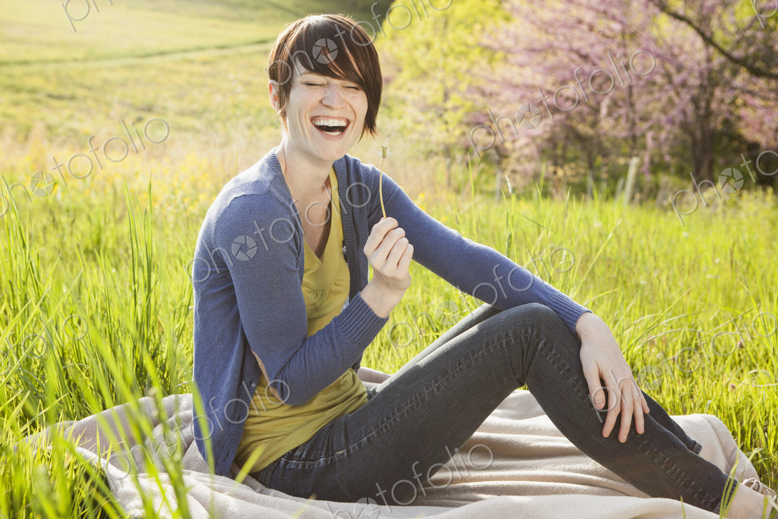 A young woman sitting in an open space, a grass field, on a blanket.