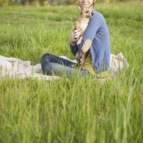 A young woman sitting in an open space, a grass field, on a blanket, holding a small… A young woman sitting in an open space, a grass field, on a blanket, holding a small…