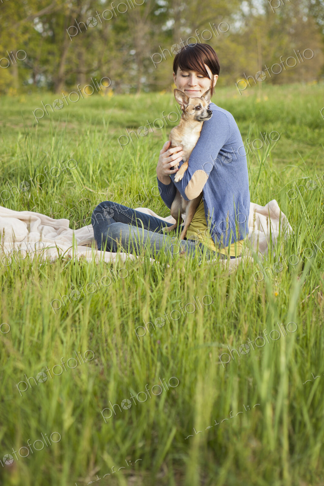 A young woman sitting in an open space, a grass field, on a blanket, holding a small…