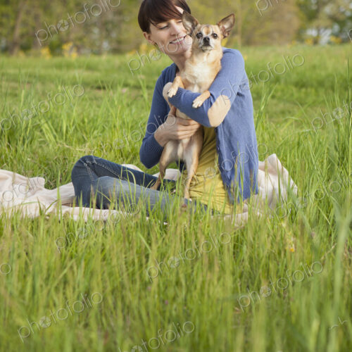A young woman sitting in an open space, a grass field, on a blanket, holding a small… A young woman sitting in an open space, a grass field, on a blanket, holding a small…