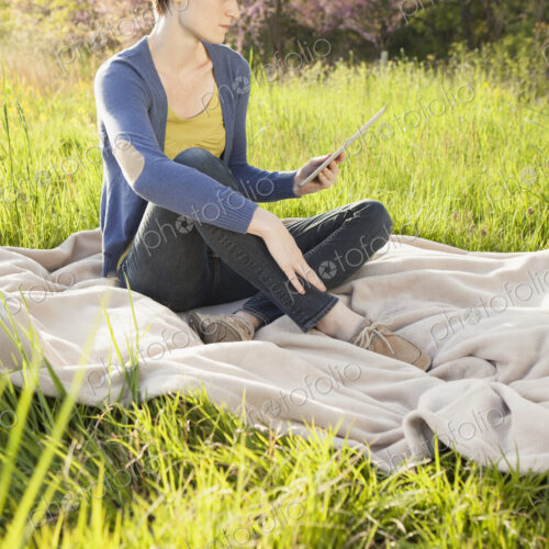 A young woman sitting in an open space, a grass field, on a blanket, holding and… A young woman sitting in an open space, a grass field, on a blanket, holding and…