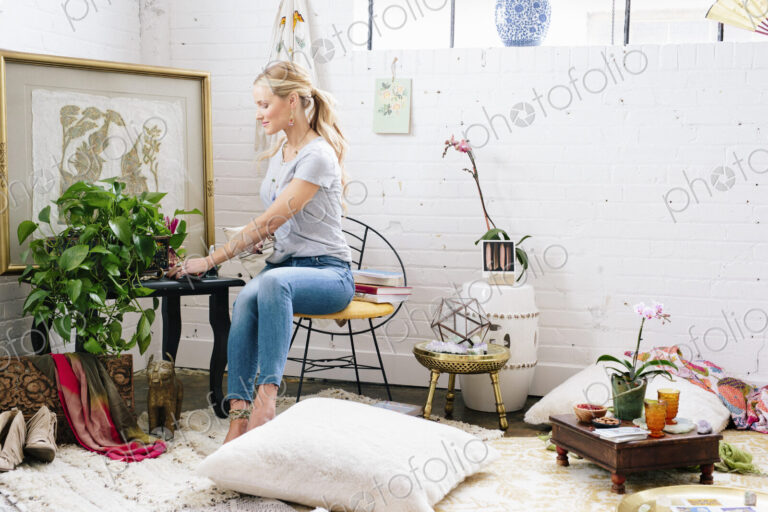 A young woman sitting on a chair in an apartment decorated with pictures and plants.