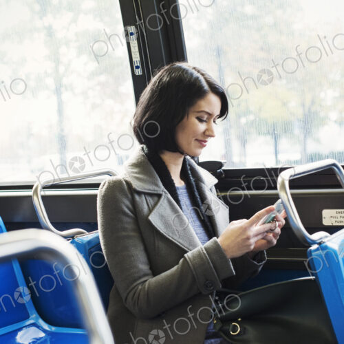 A young woman sitting on a train and looking down at a cellphone, smiling. A young woman sitting on a train and looking down at a cellphone, smiling.