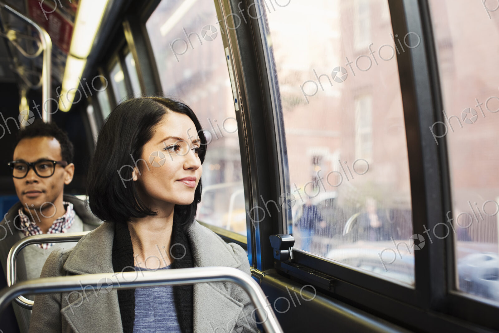 A young woman sitting on a train looking out of the window at an urban landscape, with…