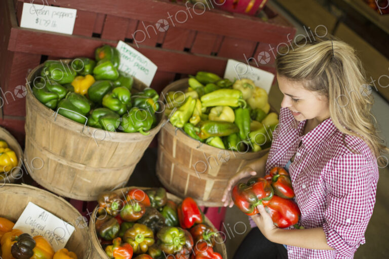 A young woman sorting different types of bell pepper for sale.