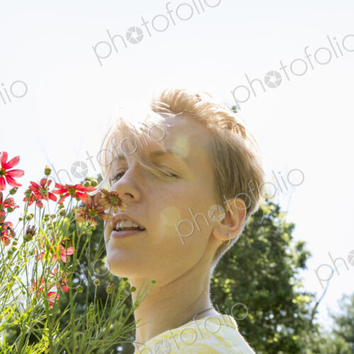 A young woman standing in a flower border, face to face with range rudbekia flowers.