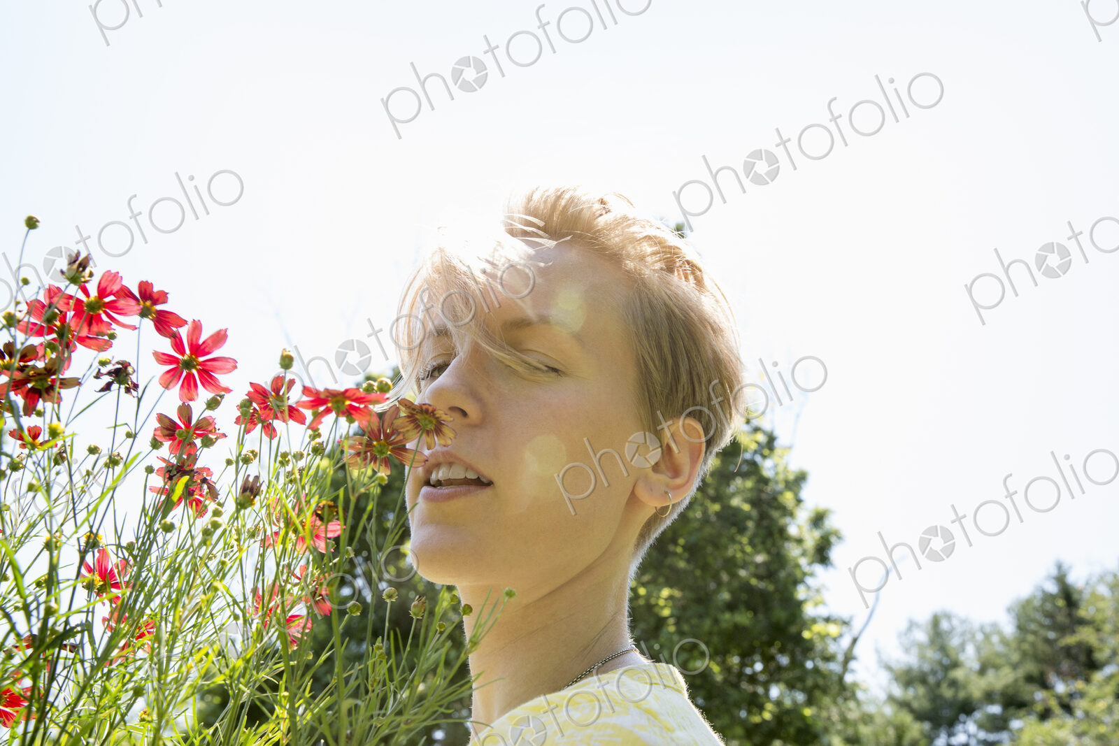 A young woman standing in a flower border, face to face with range rudbekia flowers.