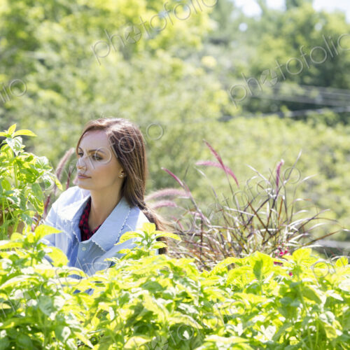 A young woman standing in a garden surrounded by growing shrubs.