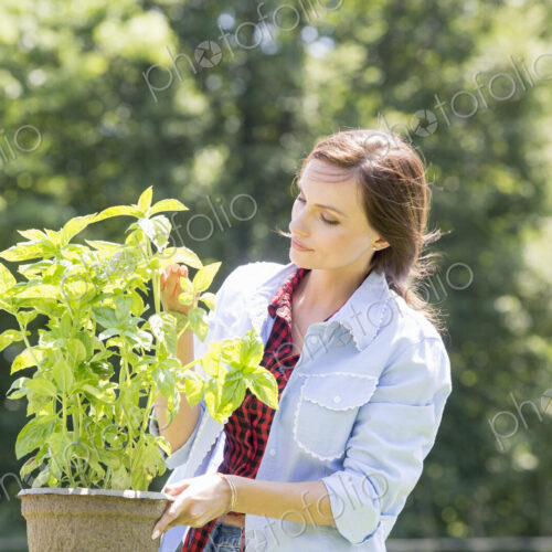A young woman standing in a garden tending a plant in a pot. A young woman standing in a garden tending a plant in a pot.