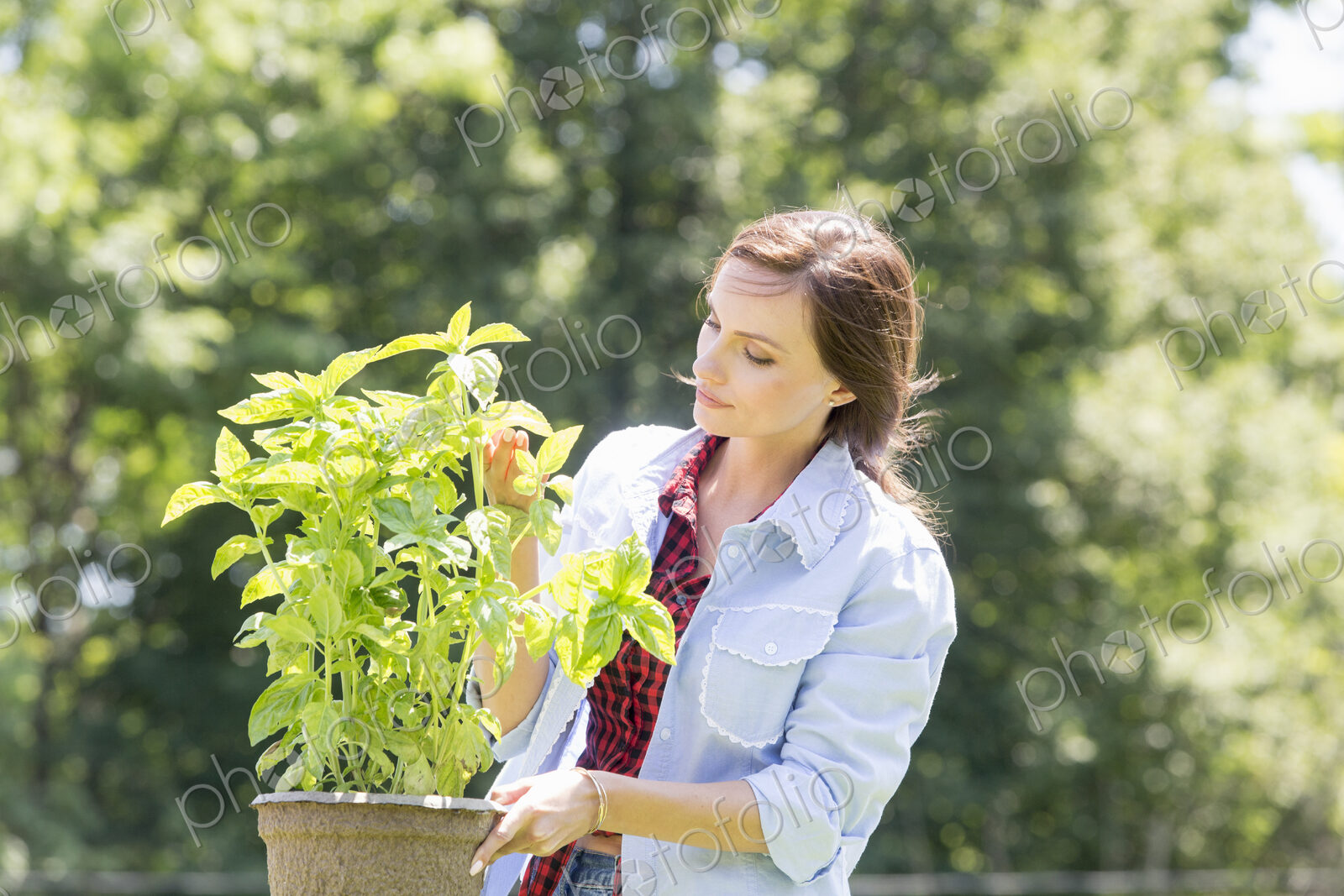 A young woman standing in a garden tending a plant in a pot.