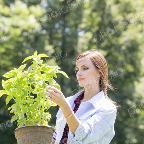 A young woman standing in a garden tending a plant in a pot. A young woman standing in a garden tending a plant in a pot.