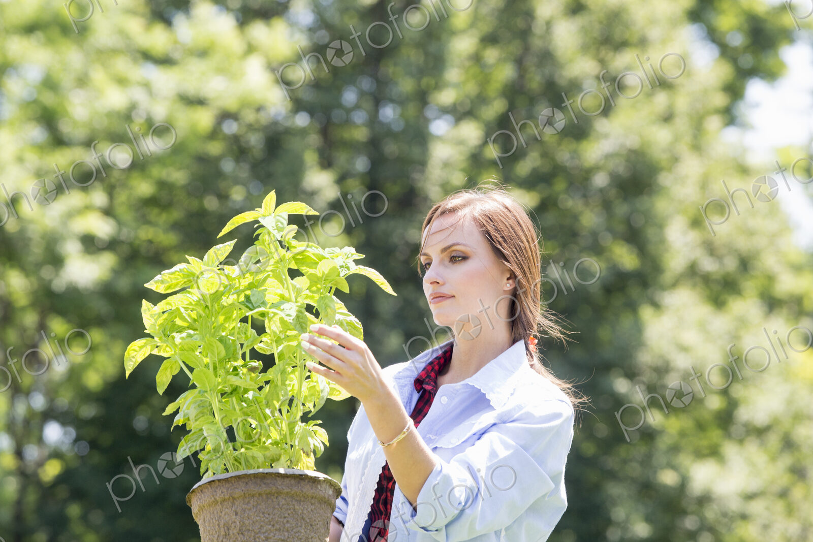 A young woman standing in a garden tending a plant in a pot.