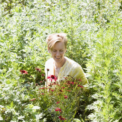 A young woman standing in a perennials bed surrounded by plants and flowers at a plant…