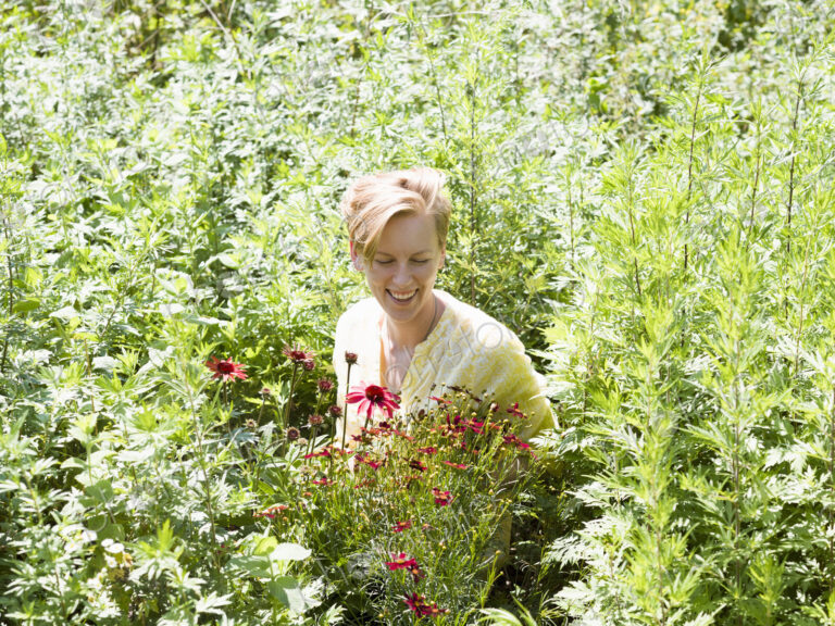 A young woman standing in a perennials bed surrounded by plants and flowers at a plant…