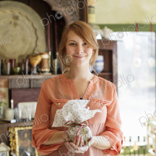 A young woman standing in a store full of antique objects, holding a tied packet with… A young woman standing in a store full of antique objects, holding a tied packet with…