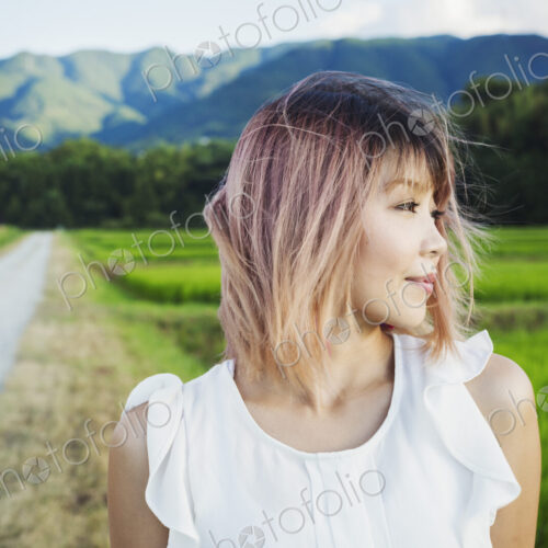 A young woman standing in open space by rice paddy fields of green shoots, and… A young woman standing in open space by rice paddy fields of green shoots, and…