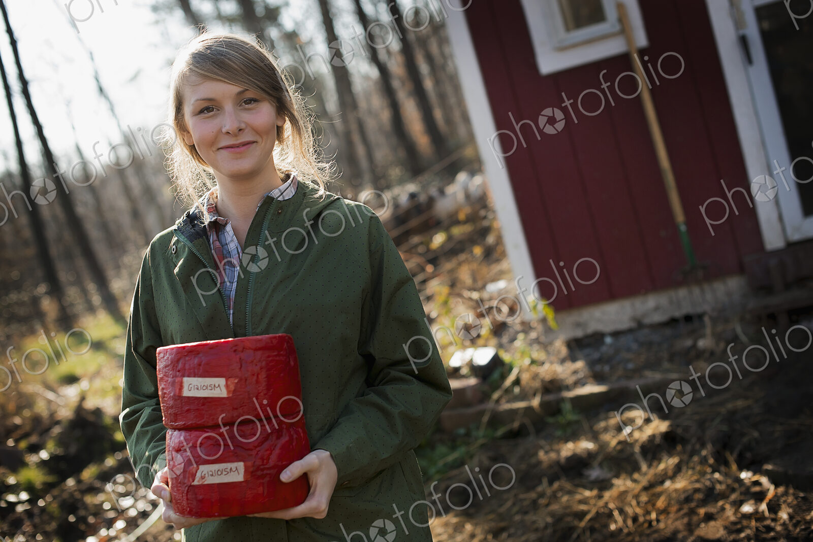 A young woman standing outside a dairy farm building holding two blocks of cheese.