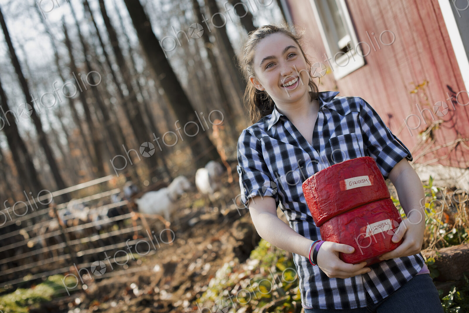 A young woman standing outside a dairy farm building holding two blocks of cheese.
