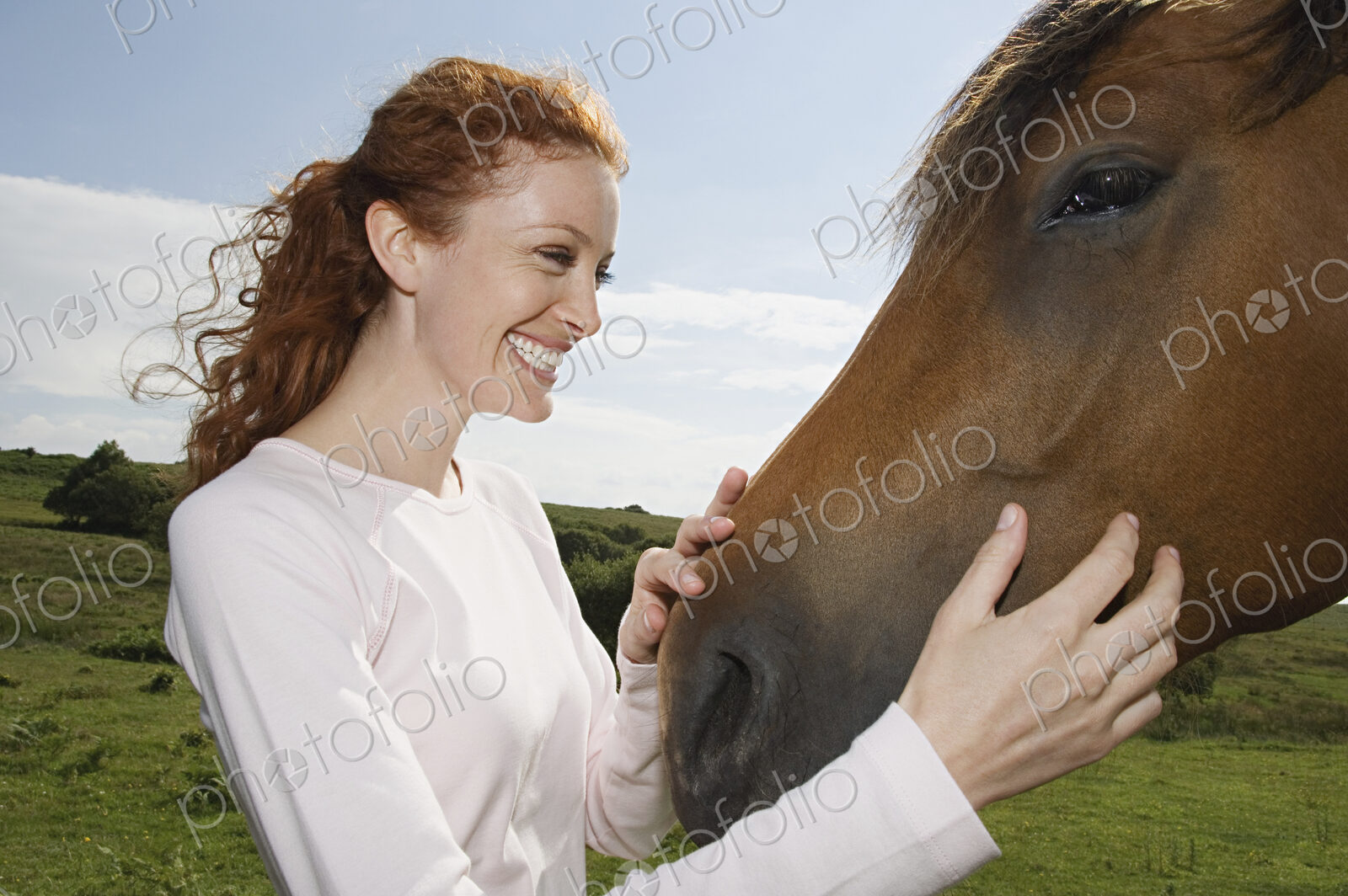A young woman stroking the muzzle of a bay horse.