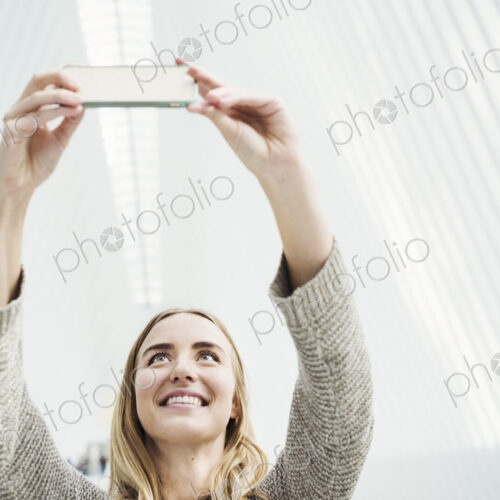 A young woman taking a photograph with her phone, taking a selfy in a large atrium. A young woman taking a photograph with her phone, taking a selfy in a large atrium.
