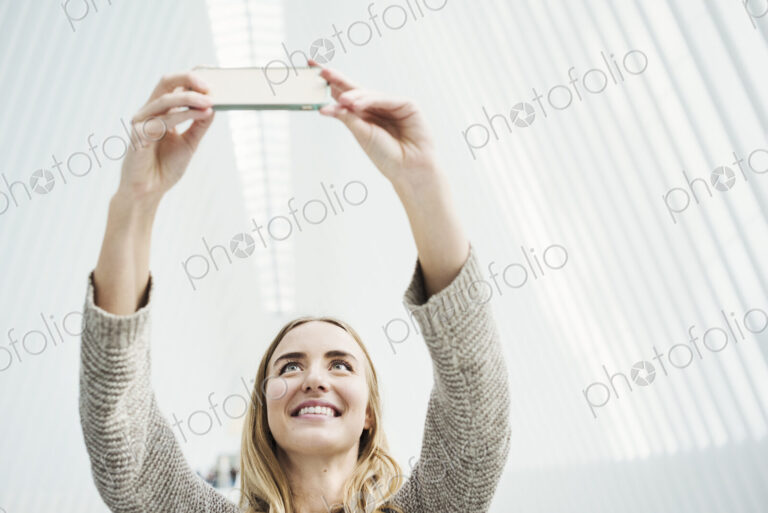 A young woman taking a photograph with her phone, taking a selfy in a large atrium.