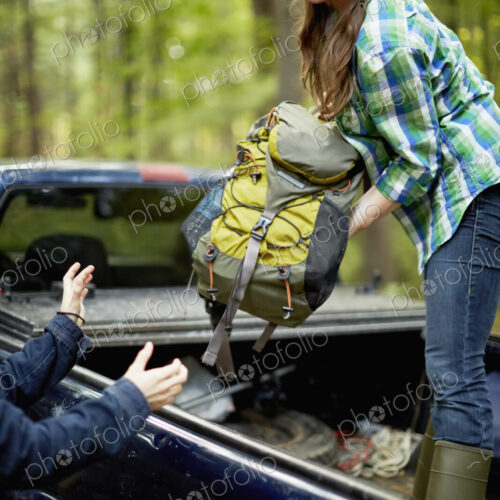 A young woman unloading rucksacks from the back of a pickup truck.