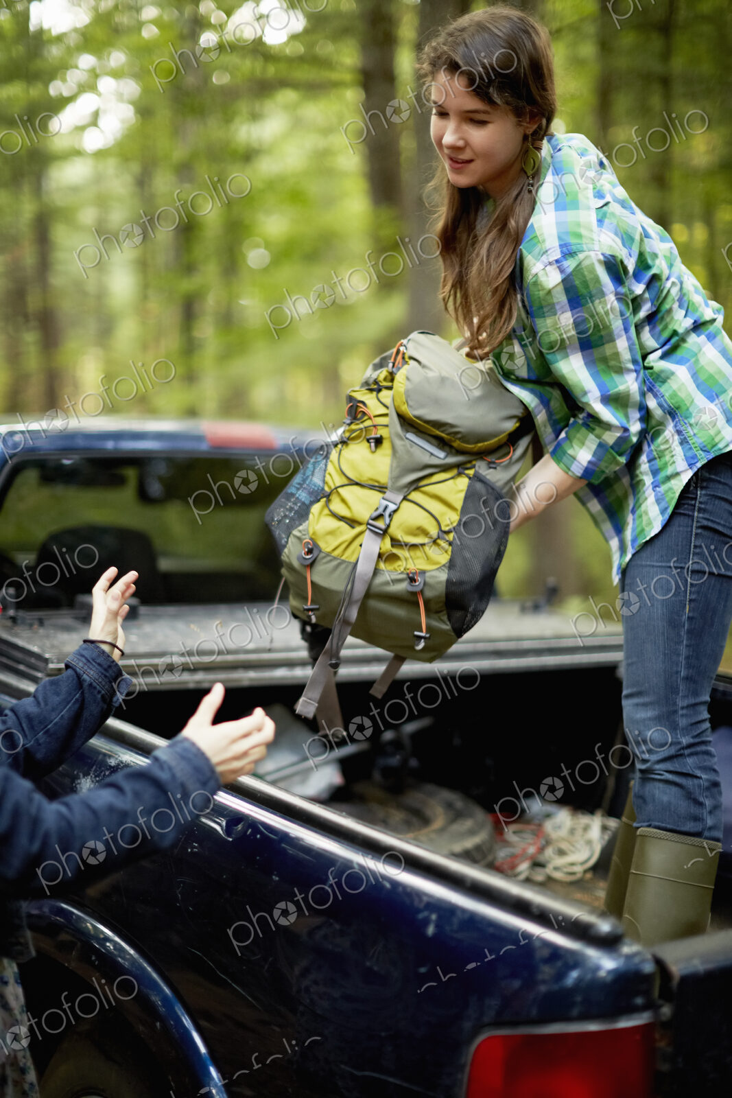 A young woman unloading rucksacks from the back of a pickup truck.