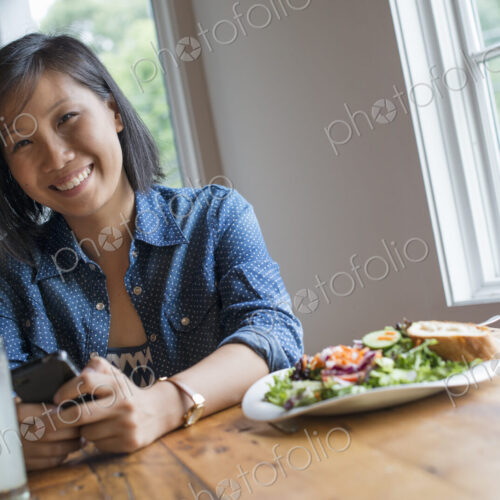 A young woman using a smart phone, seated at a table. Coffee and a sandwich. A young woman using a smart phone, seated at a table. Coffee and a sandwich.