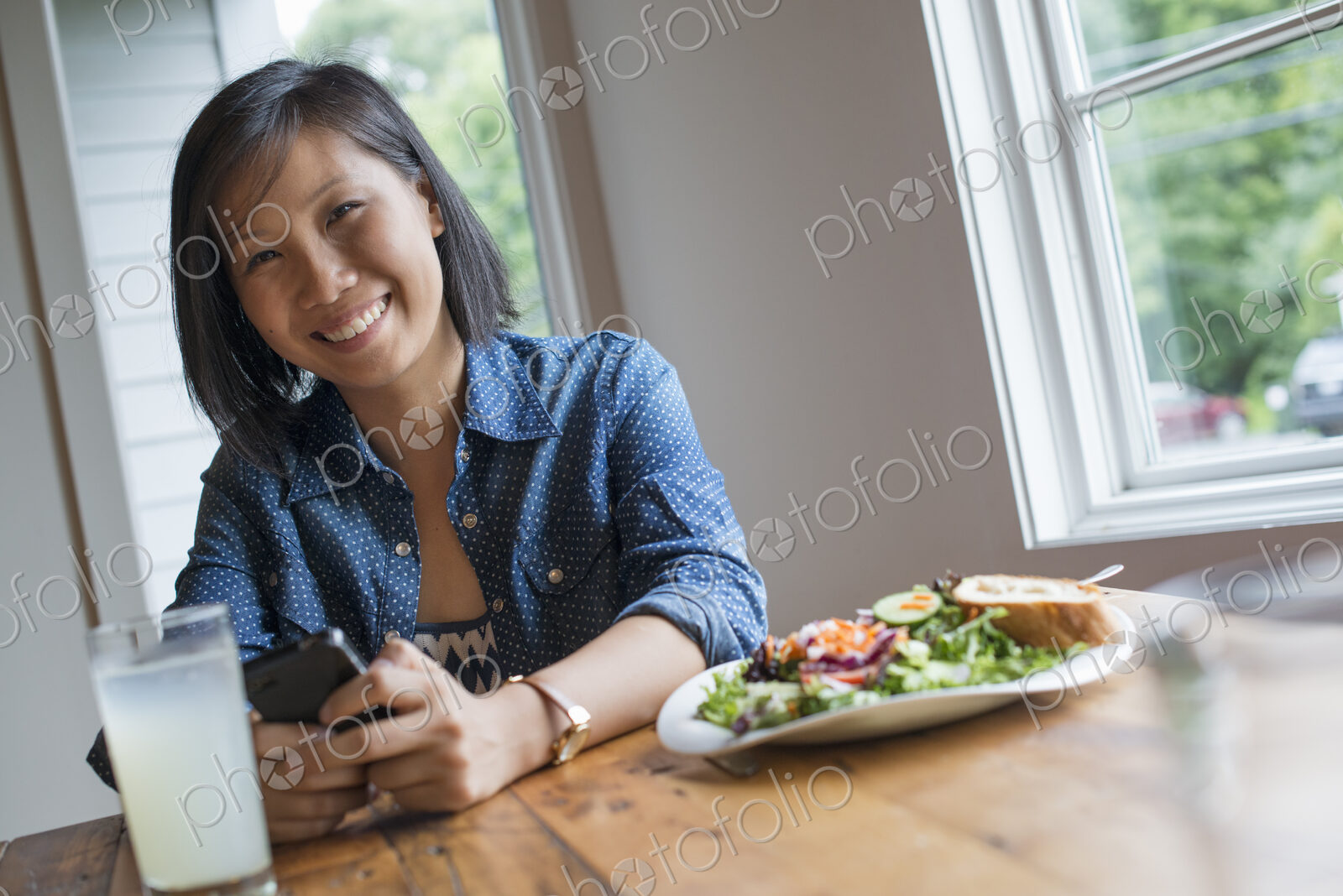A young woman using a smart phone, seated at a table. Coffee and a sandwich.