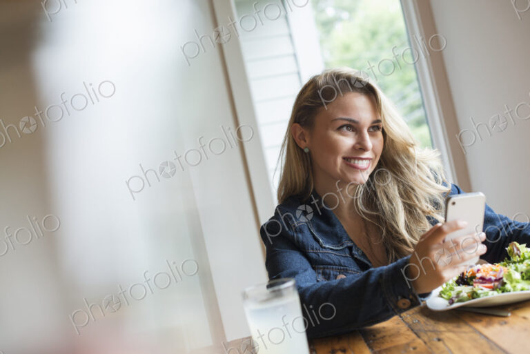 A young woman using a smart phone, seated at a table. Coffee and a sandwich.