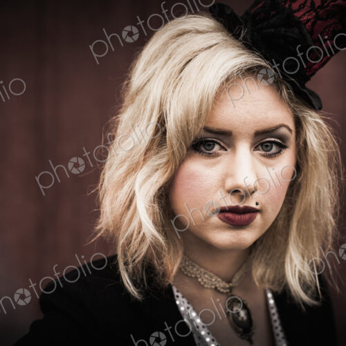 A young woman wearing a black tophat perched on the side of her head, and a black… A young woman wearing a black tophat perched on the side of her head, and a black…