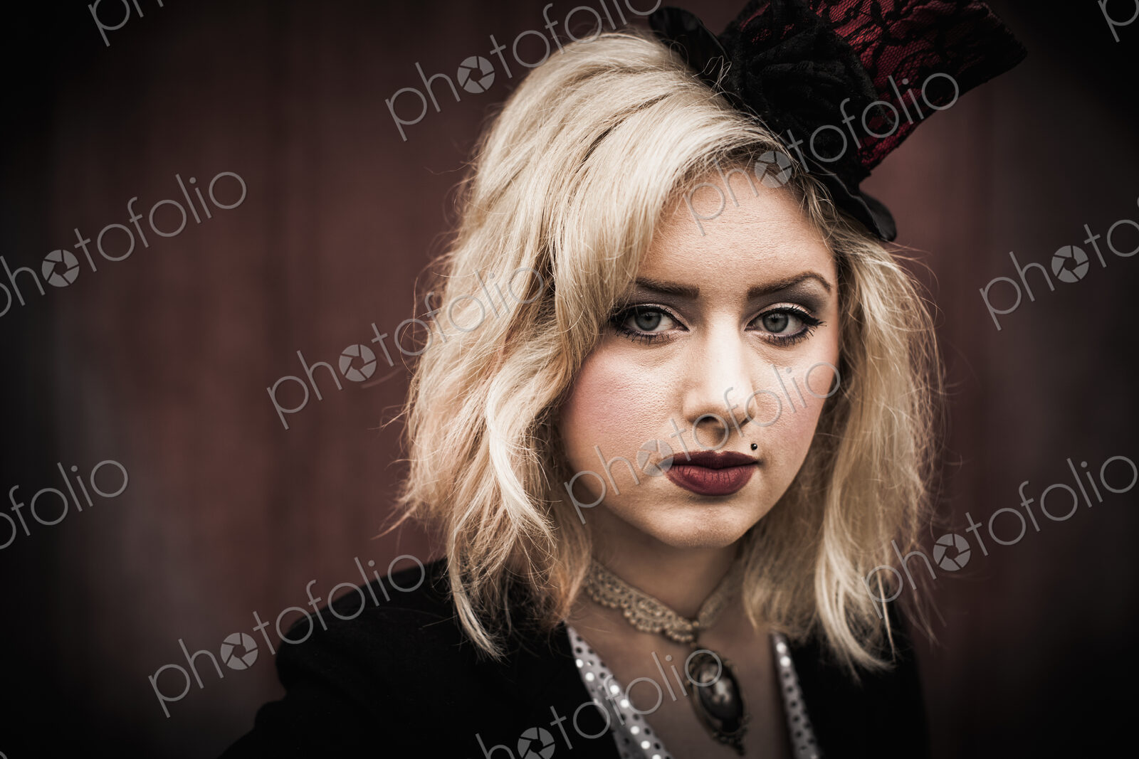 A young woman wearing a black tophat perched on the side of her head, and a black…
