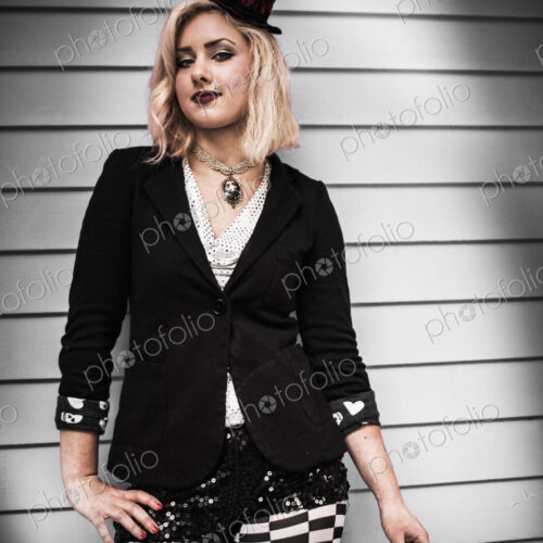 A young woman wearing a black tophat perched on the side of her head, and a black…